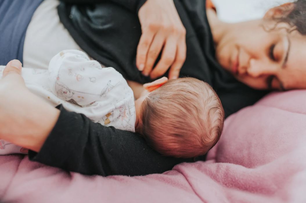 Bébé en body allongé dans un lit allaité par sa maman pendant un pic de croissance